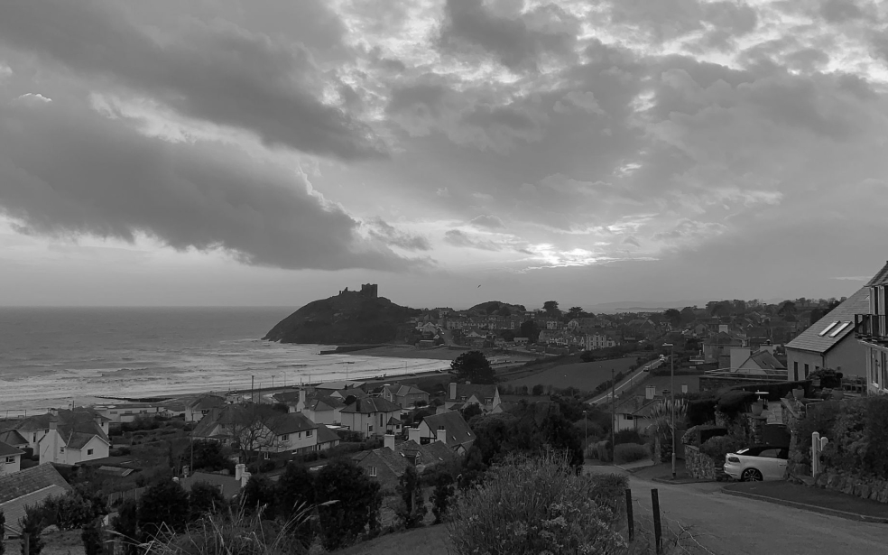 Imagen en blanco y negro que muestra una vista panorámica de un pueblo costero situado en una colina que desciende hacia el mar.